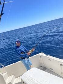 An angler actively reeling in a catch while fishing on a boat in open water, showcasing the excitement of deep-sea fishing.