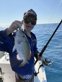 A young angler proudly displaying a freshly caught fish while fishing on a sunny day at sea.