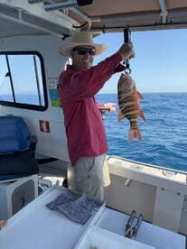 An angler proudly displaying a colorful Grouper while fishing on a charter boat in clear blue waters.