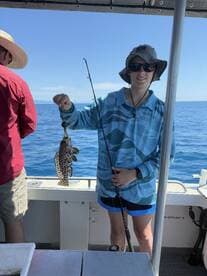 A young angler proudly displaying a Spotted Grouper while fishing on a boat in clear blue waters.