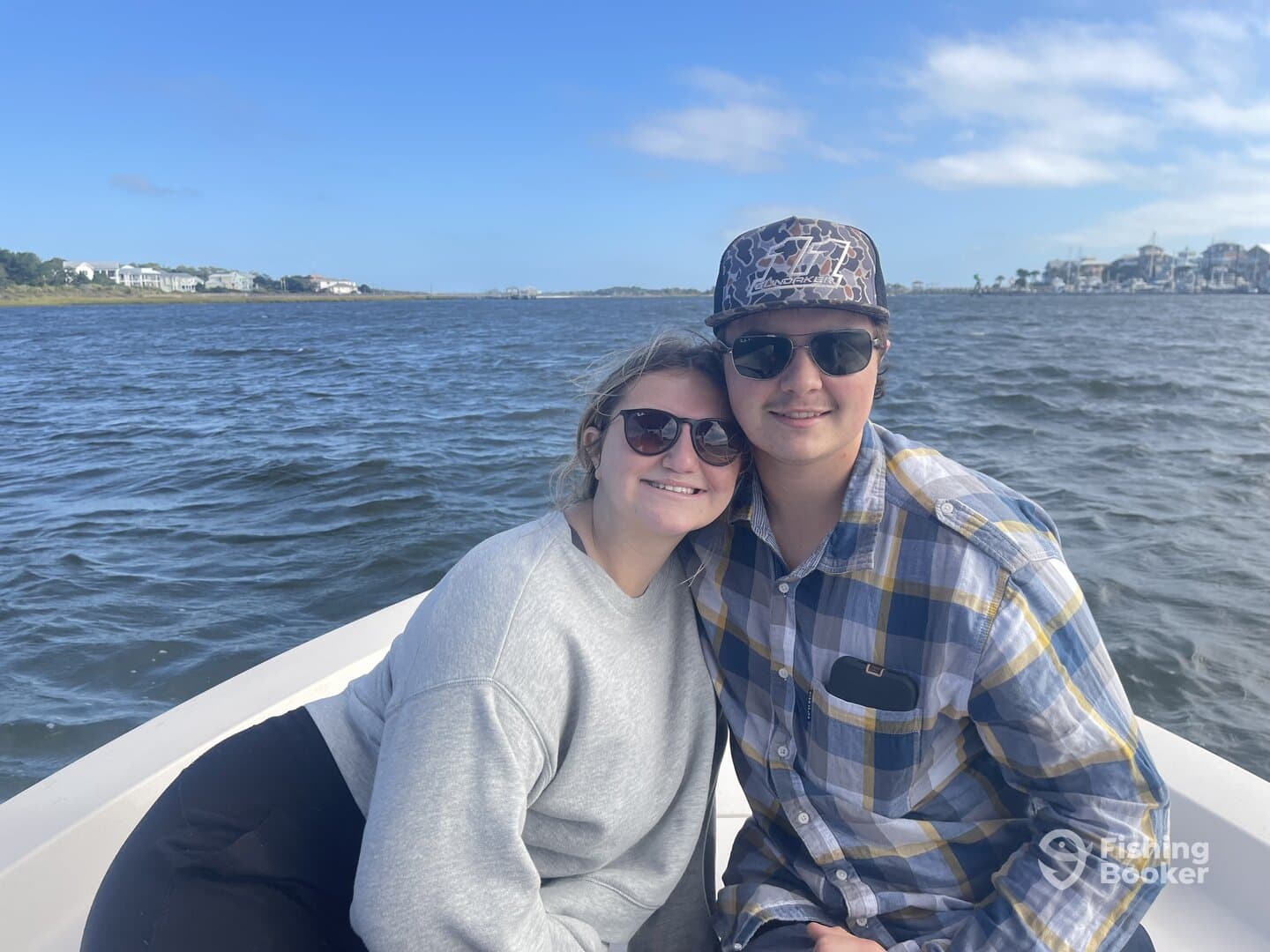 A couple enjoying a scenic boat ride, smiling together against a backdrop of waterfront homes.