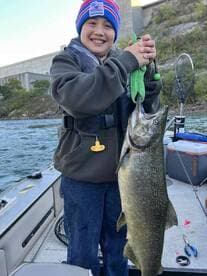 Young angler proudly holding a large fish while fishing on a boat, showcasing a successful catch in a scenic environment.