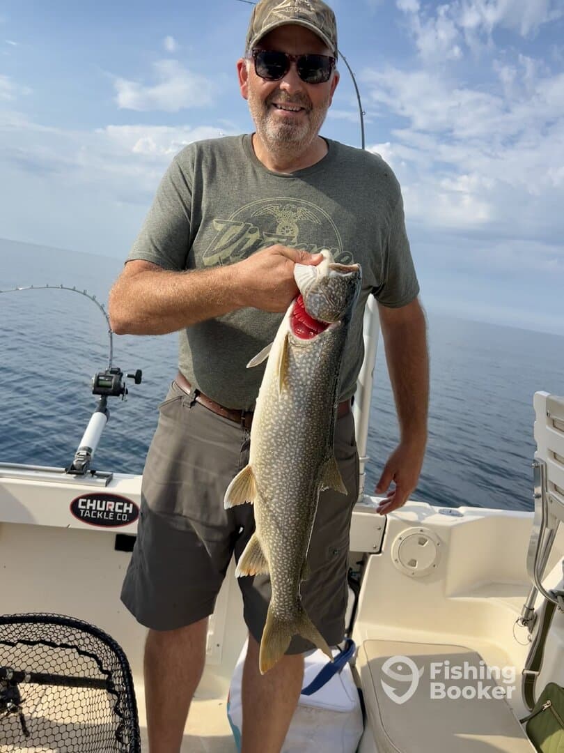 An angler proudly displaying a large Lake Trout while fishing on a boat in open waters.