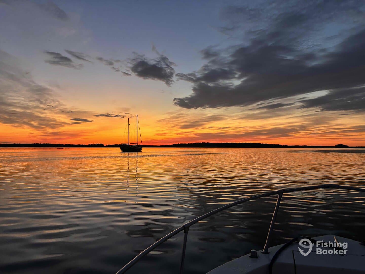 A serene sunset view over calm waters with a sailboat silhouetted against the vibrant sky, showcasing a peaceful fishing environment.