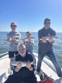 A family of four proudly displaying their catch of Speckled Trout while enjoying a day on the water.