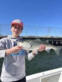 A young angler proudly displaying a striped bass while fishing on a sunny day.