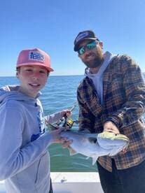A young angler and an adult proudly displaying a caught fish while fishing in open waters, showcasing a successful day on the boat.