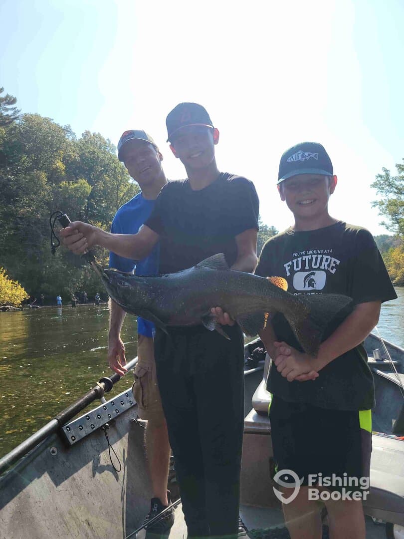 A family proudly displays a large trout while fishing on a scenic river, showcasing a successful day on the water.