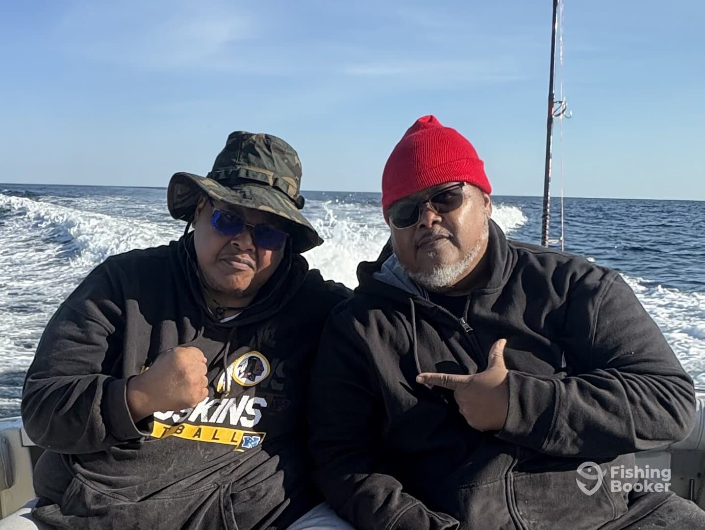 Two anglers enjoying a day on the water, seated inside the boat with a scenic ocean backdrop.