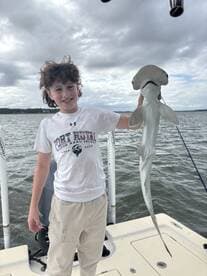 A young angler proudly displaying a caught Hammerhead Shark while fishing from a boat in coastal waters.