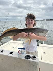A young angler proudly displaying a large Redfish while fishing on a boat, showcasing a successful day on the water.