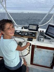 A young girl confidently steering the boat from the helm, showcasing the interior features and a scenic view of the coastline.