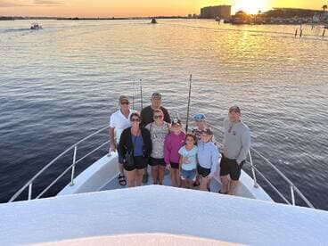 A cheerful group of family members posing on the bow of a boat during sunset, showcasing a beautiful fishing environment.