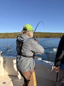 An angler reeling in a catch while fishing on a serene lake, surrounded by autumn foliage.