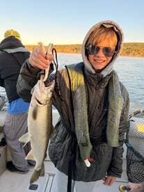 A young angler proudly displaying a caught fish while fishing on a scenic lake, showcasing the excitement of a family fishing trip.