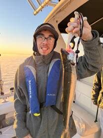 An angler proudly displaying a freshly caught fish aboard a boat during a sunset fishing trip.