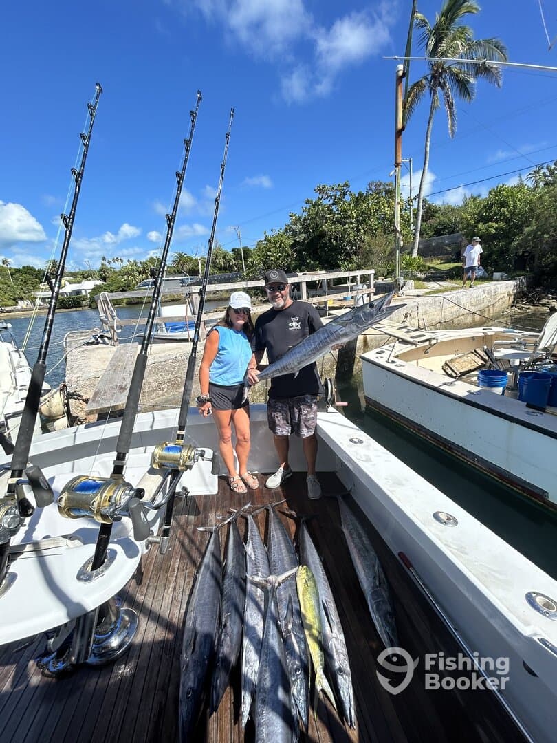 Two anglers proudly displaying their catch of multiple Mahi Mahi and Wahoo on the deck of a sportfishing boat in a tropical setting.