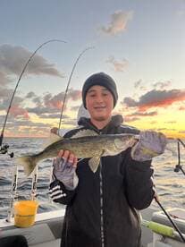 A young angler proudly displaying a Walleye while fishing during sunset on a boat.