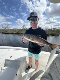 Angler displaying a Redfish while on a fishing charter in a scenic waterway, showcasing the thrill of the catch.