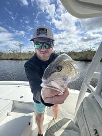 Angler proudly displaying a large Snook while fishing on a boat in a scenic waterway.