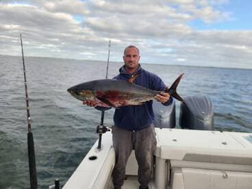 Angler proudly displaying a large Tuna while aboard a fishing boat, showcasing a successful day on the water.
