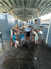 A family proudly displaying their catch of Redfish at a marina, showcasing a fun day of fishing together.