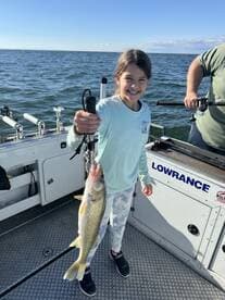 A young angler proudly displaying a Walleye while fishing on a boat, enjoying a sunny day on the water.