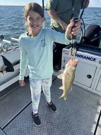 A young angler joyfully displaying a freshly caught Walleye on a fishing charter, with a scenic water backdrop.
