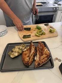 A person preparing a meal with grilled fish, including fillets and vegetables, in a kitchen setting.