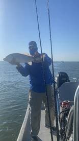Angler proudly displaying a large Redfish while fishing on a boat in open waters.