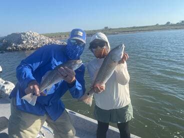 Two anglers proudly displaying their catches of Redfish while on a boat in a coastal fishing environment.