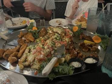 A group enjoying a large platter of seafood dishes at a restaurant, featuring a variety of fried fish and garnishes.