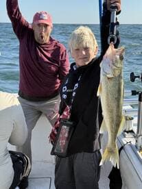 A young angler proudly displaying a Walleye while fishing on a boat, with an excited adult in the background celebrating the catch.