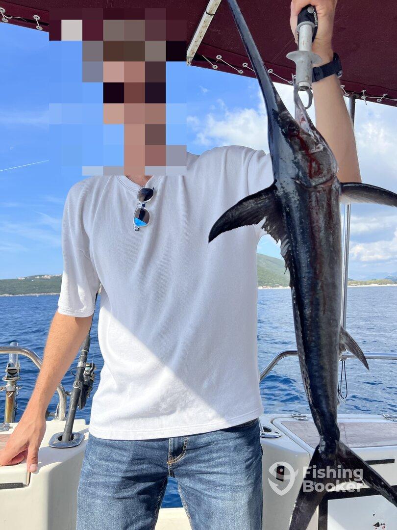 Angler holding a large Swordfish on a boat, showcasing a successful deep-sea fishing trip.
