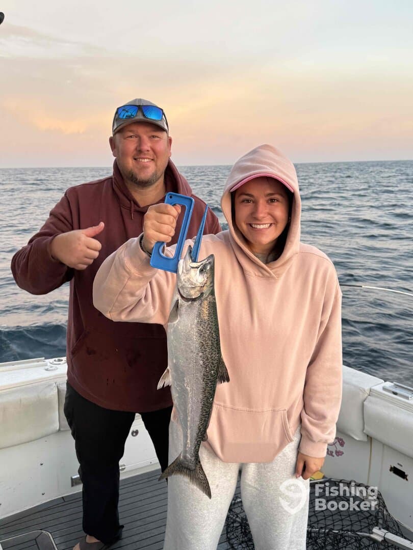 Two anglers proudly displaying a large trout caught during a sunset fishing trip on a charter boat.
