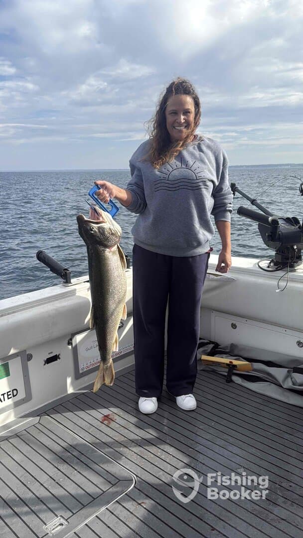 An angler proudly displaying a large Walleye while fishing on a boat, showcasing a successful catch in a scenic water environment.