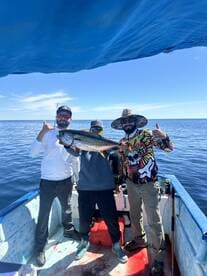 Three anglers proudly displaying a large fish on a small boat while fishing in open waters.