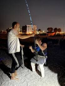Two anglers engaged in a night fishing session on the beach, with one preparing to reel in a catch while the other assists.
