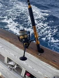 Close-up of a fishing rod and reel mounted on the side of a boat, with ocean waves in the background, showcasing the fishing setup.