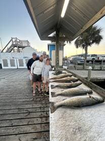 A family group proudly posing with their catch of several large Speckled Trout displayed on a cleaning table at the dock.