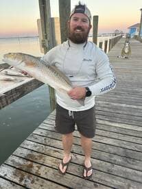 An angler proudly displaying a large Redfish on the dock, showcasing a successful fishing trip in a coastal environment.