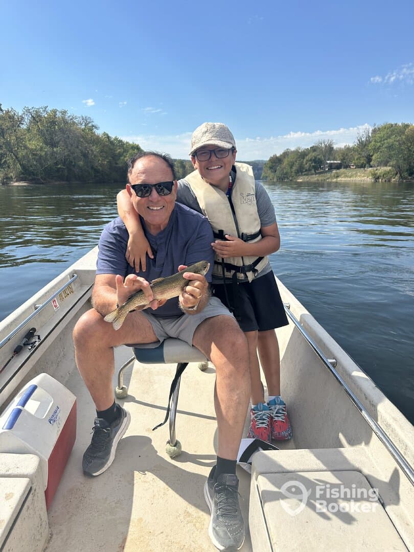 A young boy and his father proudly displaying a freshly caught Rainbow Trout while enjoying a day on the water.