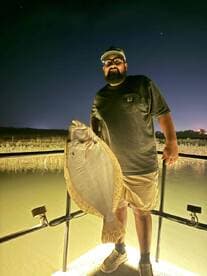 Angler proudly displaying a large Flounder at night, showcasing a successful fishing trip.