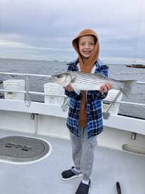 A young angler proudly displaying a striped bass while fishing on a boat, showcasing a successful outing.