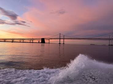 A stunning sunset view of a bridge over calm waters, captured from a boat, showcasing the tranquil fishing environment.