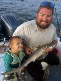 A young boy and an adult proudly displaying a caught shark while fishing on a boat, showcasing a memorable family fishing experience.
