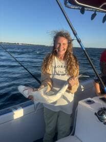 An angler proudly displaying a caught shark while fishing on a boat, showcasing a sunny day on the water.