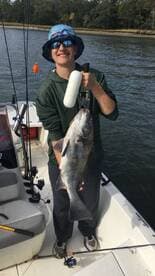 A young angler proudly displaying a large Black Drum while fishing from a boat in a calm waterway.