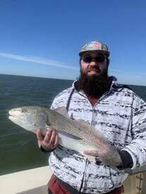 Angler proudly displaying a large Speckled Trout while fishing on a boat in open waters.