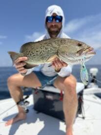 An angler proudly displaying a large Grouper caught while fishing offshore, showcasing the excitement of a successful day on the water.